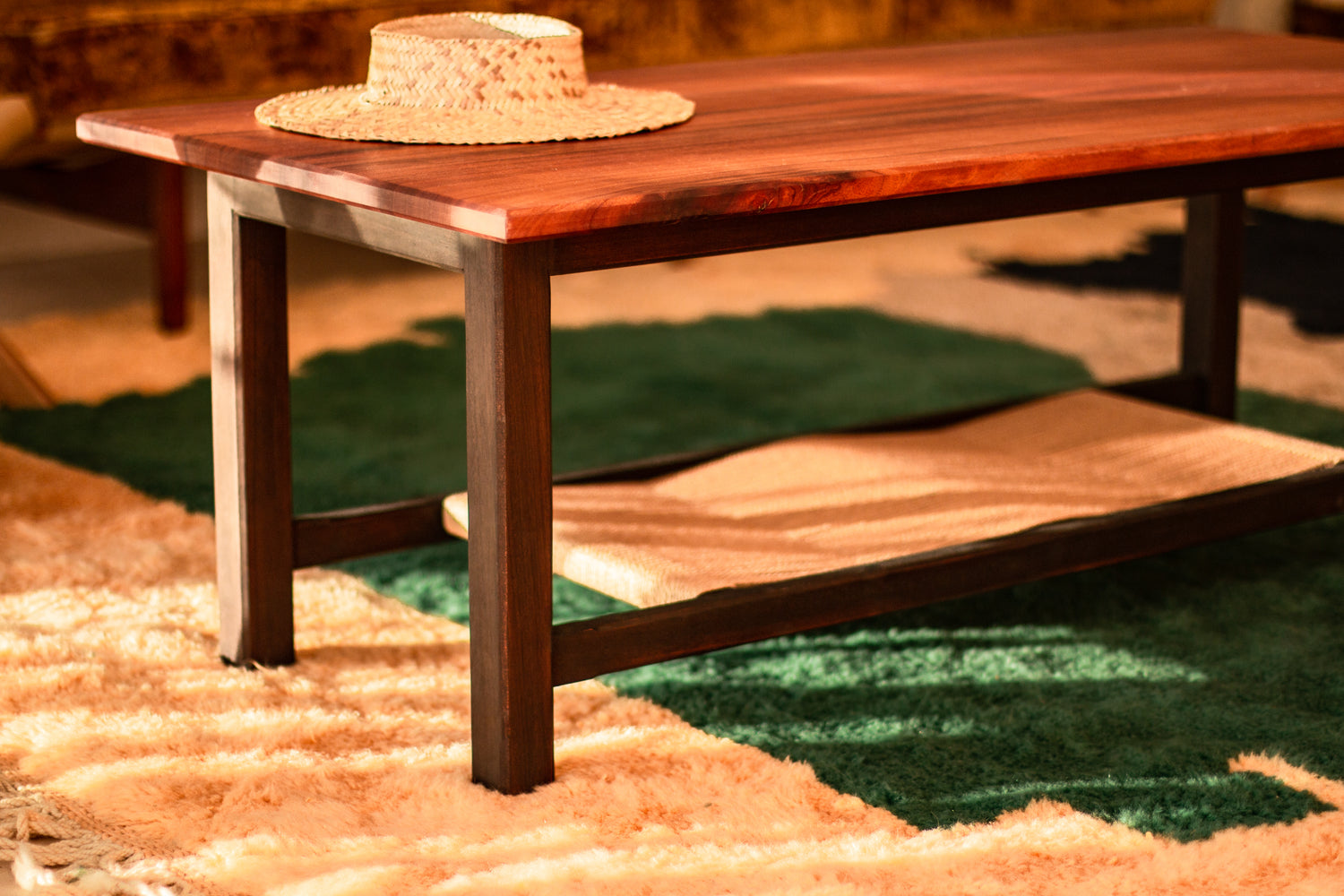 Mahogany Hibal Coffee Table sits on a geometric green and cream rug, with woven hat on top.