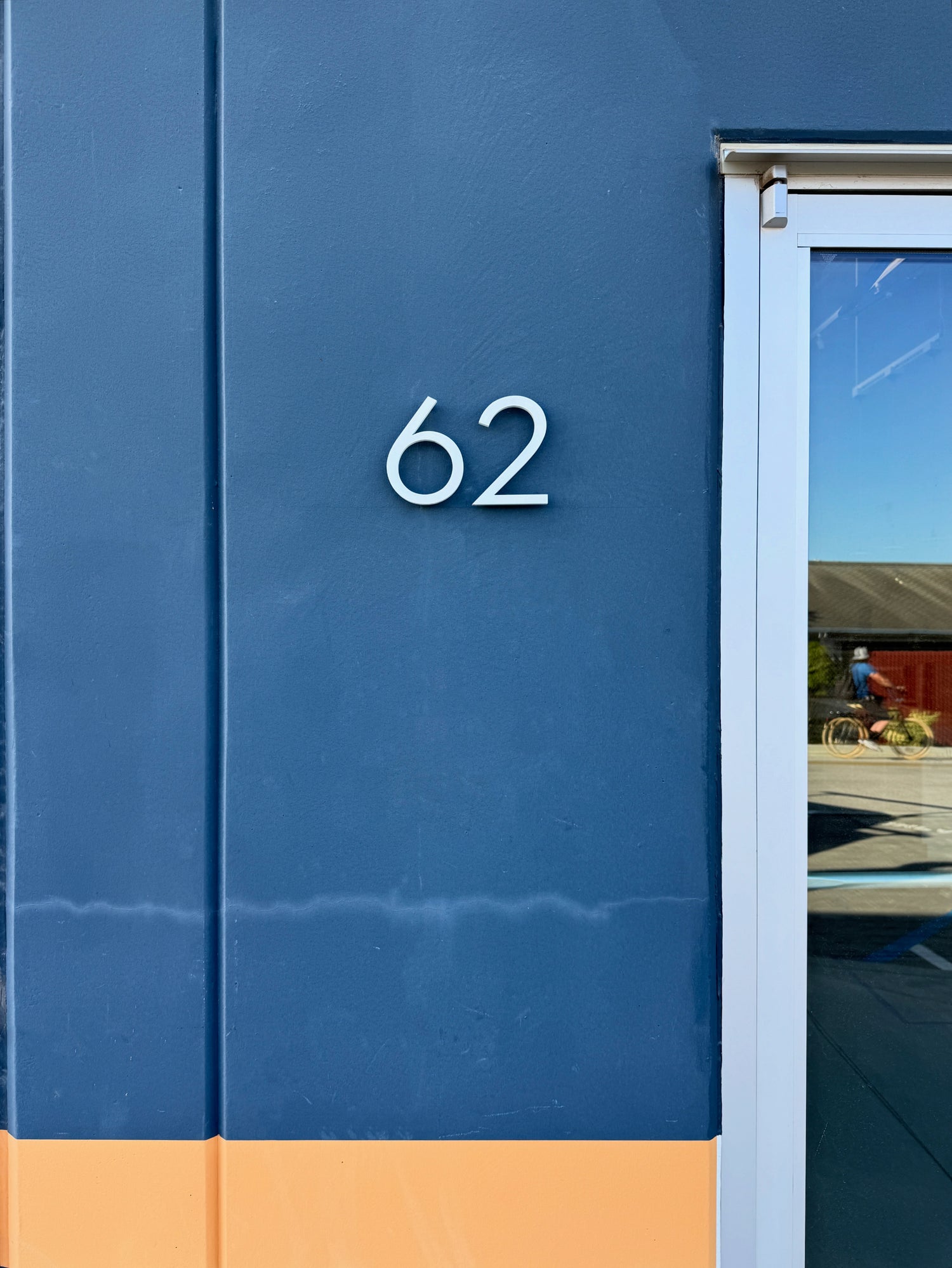number '62' on a blue wall with a reflection of a person riding a bike.