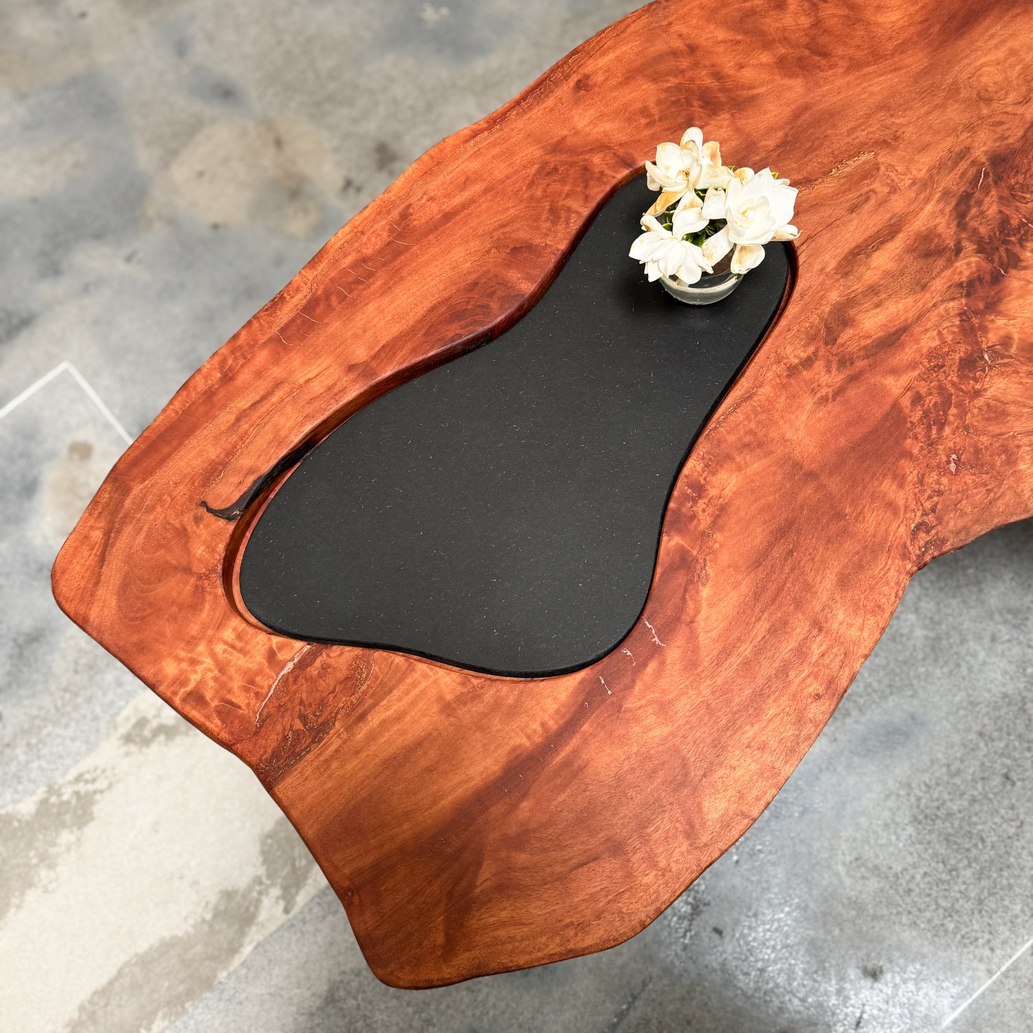 Wooden coffee table with an inset black panel and gardenia flowers on a concrete floor.