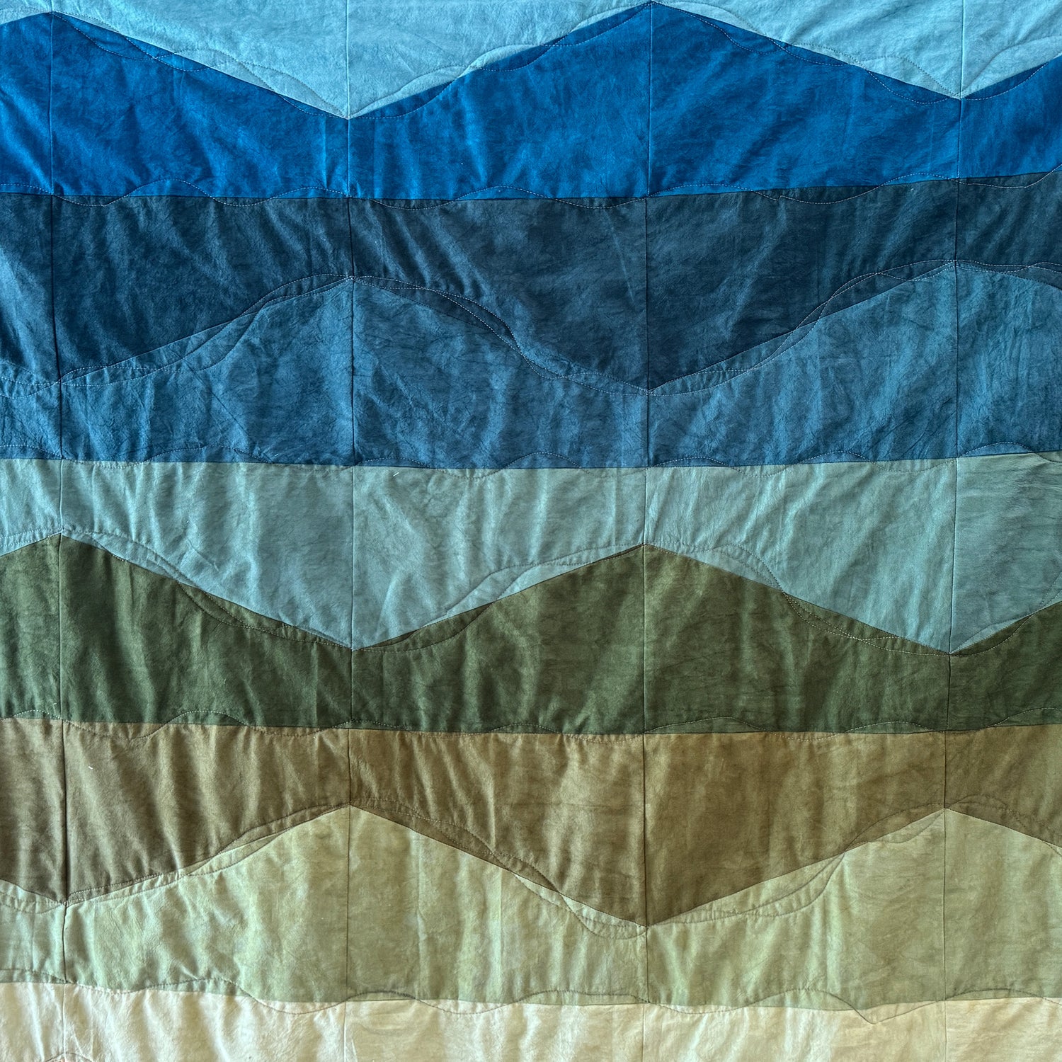 Quilt with wavy pattern in blue, green, and beige colors