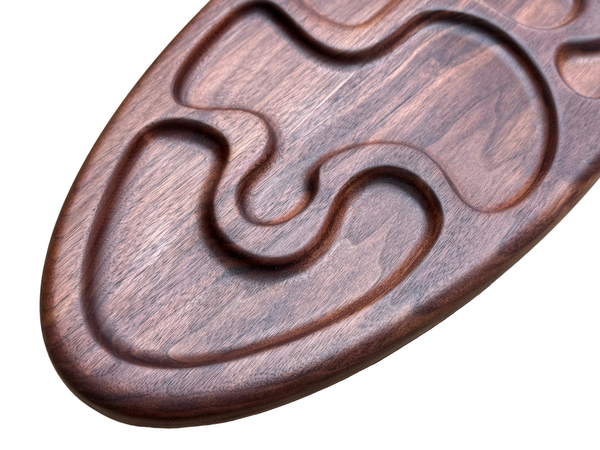 A close-up of a dark brown wooden tray (made of walnut) with carved wavy pattern.